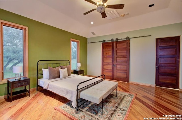 bedroom with light wood-type flooring, a raised ceiling, ceiling fan, and a barn door