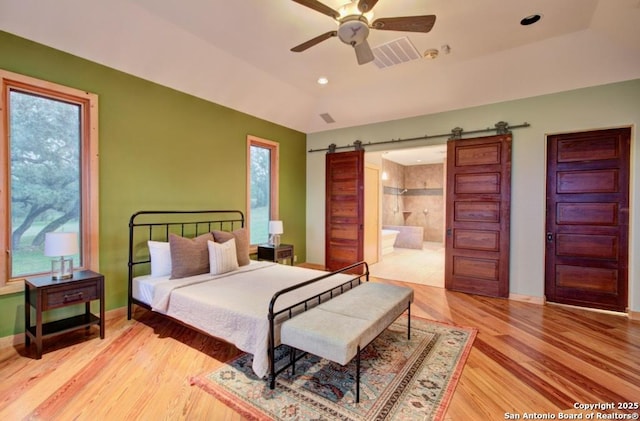 bedroom featuring ceiling fan, a barn door, light hardwood / wood-style floors, and connected bathroom