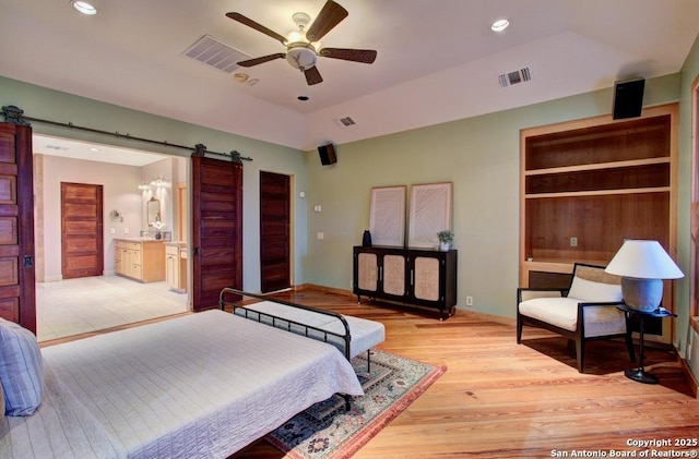 bedroom featuring ensuite bathroom, light hardwood / wood-style floors, ceiling fan, a barn door, and a raised ceiling