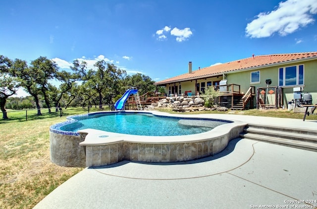 view of pool featuring a lawn, a wooden deck, and a water slide