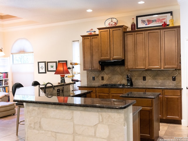 kitchen featuring tasteful backsplash, light tile patterned flooring, a kitchen island with sink, and ventilation hood