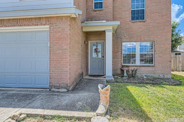 view of exterior entry with a garage, a yard, and brick siding