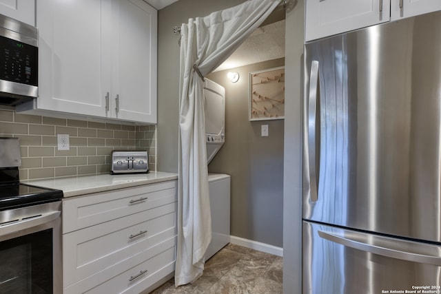 kitchen with light tile patterned flooring, appliances with stainless steel finishes, backsplash, white cabinets, and stacked washer / drying machine