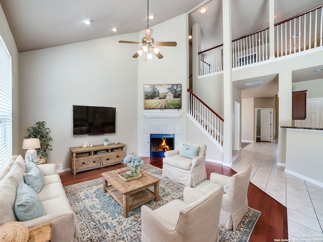 living room featuring a tiled fireplace, ceiling fan, a high ceiling, and light hardwood / wood-style floors