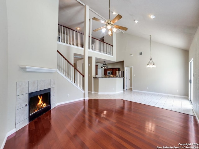 unfurnished living room with hardwood / wood-style flooring, high vaulted ceiling, a fireplace, and ceiling fan with notable chandelier