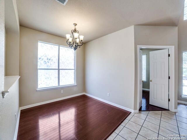 spare room with a textured ceiling, light hardwood / wood-style floors, and a notable chandelier