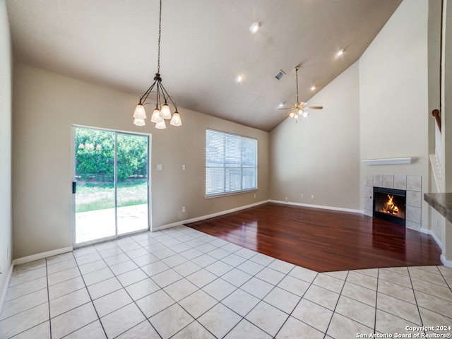 unfurnished living room featuring ceiling fan with notable chandelier, light wood-type flooring, high vaulted ceiling, and a tiled fireplace