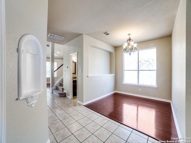 tiled empty room with a textured ceiling and a chandelier