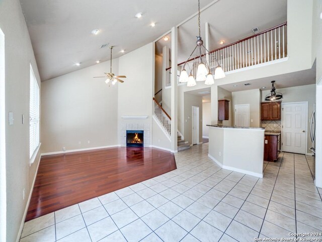 unfurnished living room featuring hardwood / wood-style floors, ceiling fan, a tile fireplace, and high vaulted ceiling