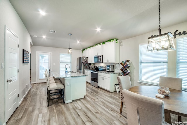 kitchen with stainless steel appliances, light hardwood / wood-style flooring, light stone countertops, a kitchen island with sink, and a breakfast bar