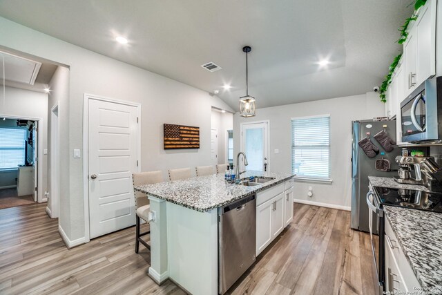 kitchen with light hardwood / wood-style flooring, hanging light fixtures, an island with sink, white cabinetry, and appliances with stainless steel finishes