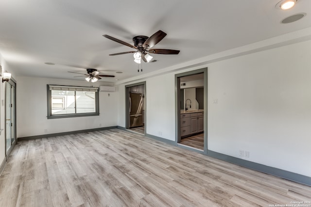 unfurnished bedroom featuring light wood-type flooring, a wall mounted air conditioner, ensuite bathroom, stainless steel refrigerator, and sink