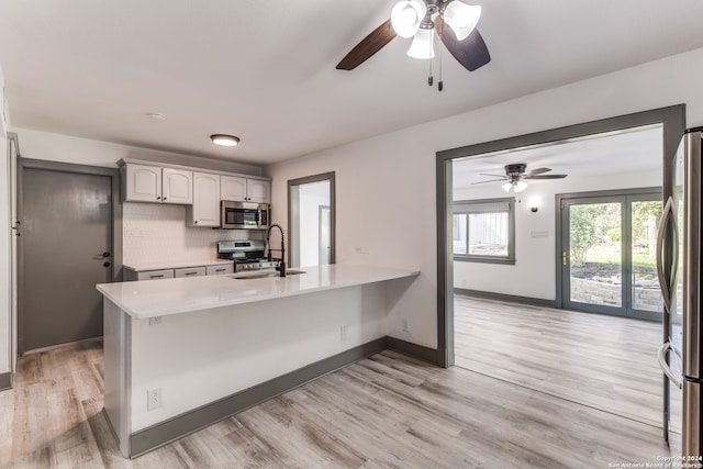 kitchen featuring decorative backsplash, ceiling fan, appliances with stainless steel finishes, kitchen peninsula, and light hardwood / wood-style floors