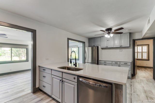 kitchen featuring stainless steel appliances, decorative backsplash, gray cabinets, sink, and light hardwood / wood-style flooring