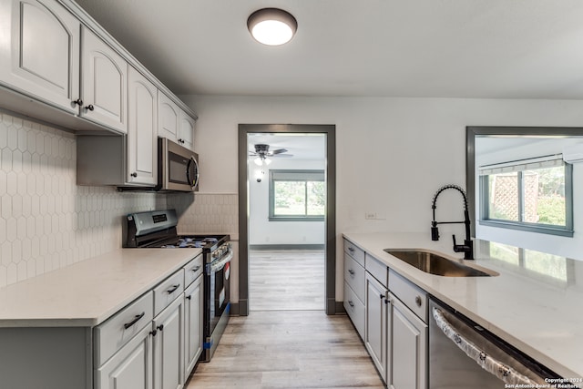 kitchen with stainless steel appliances, ceiling fan, sink, tasteful backsplash, and light hardwood / wood-style flooring