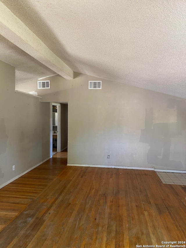 empty room with wood-type flooring, a textured ceiling, and lofted ceiling