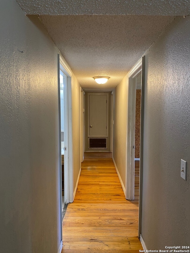 hall featuring a textured ceiling and light hardwood / wood-style floors