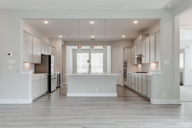 kitchen featuring baseboards, light countertops, appliances with stainless steel finishes, backsplash, and a center island with sink