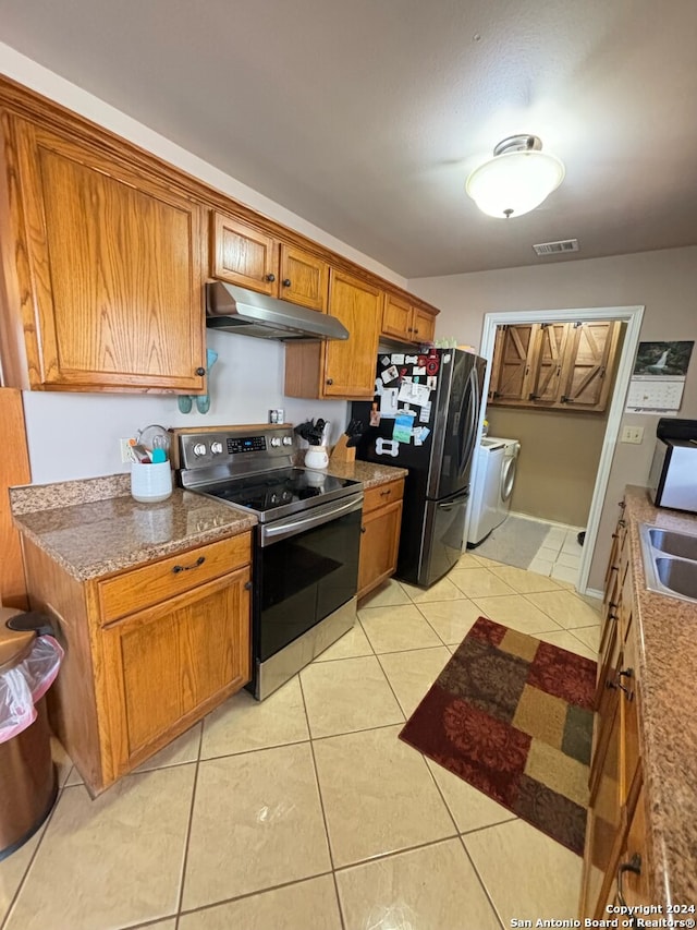 kitchen featuring light tile patterned floors, appliances with stainless steel finishes, washing machine and dryer, and under cabinet range hood