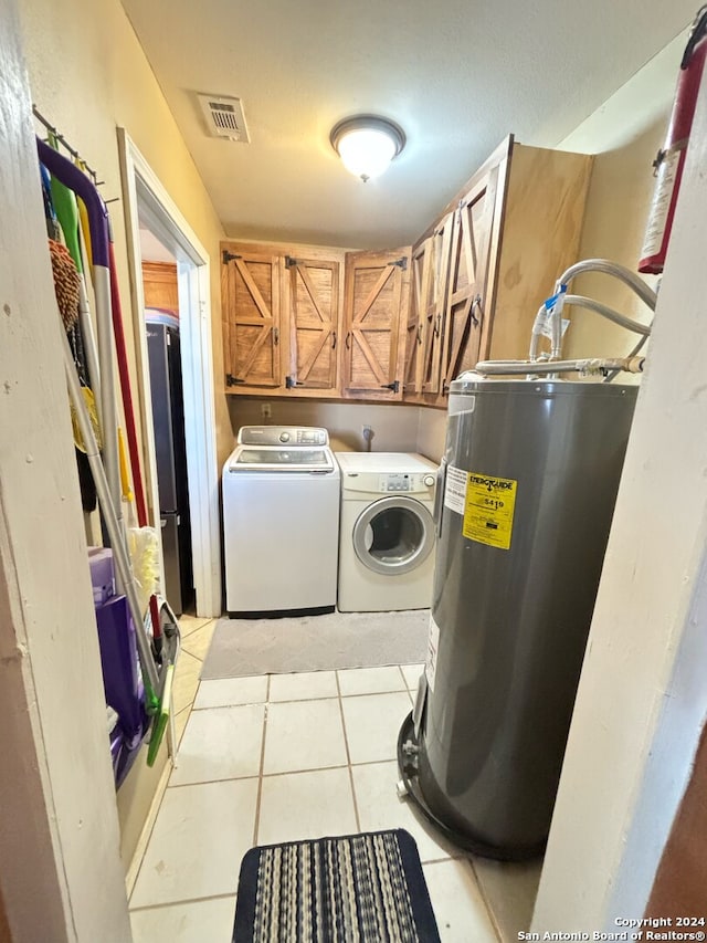 washroom featuring light tile patterned floors, electric water heater, visible vents, independent washer and dryer, and cabinet space