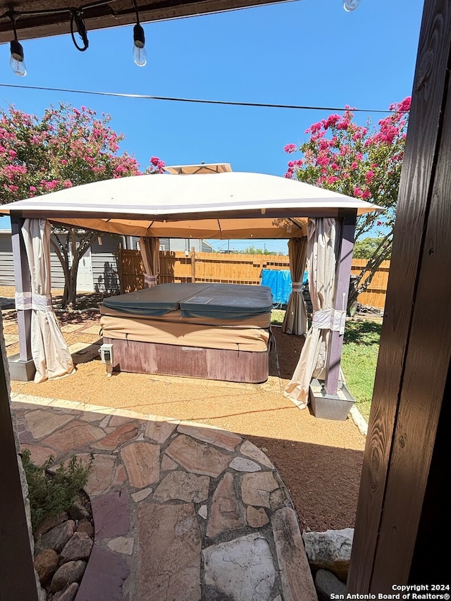 view of patio / terrace featuring a carport, fence, a covered hot tub, and a gazebo