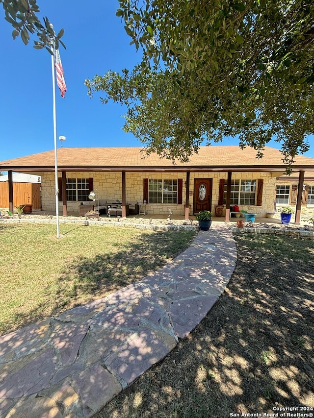 ranch-style house featuring stone siding, a front lawn, a patio, and fence