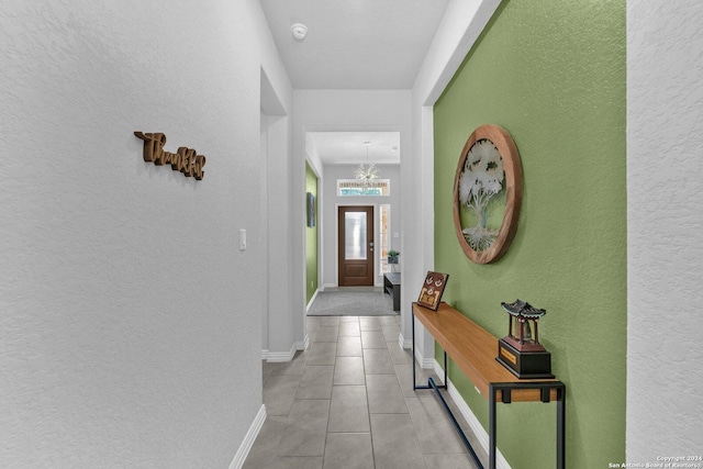 foyer featuring a textured wall, a notable chandelier, baseboards, and light tile patterned floors