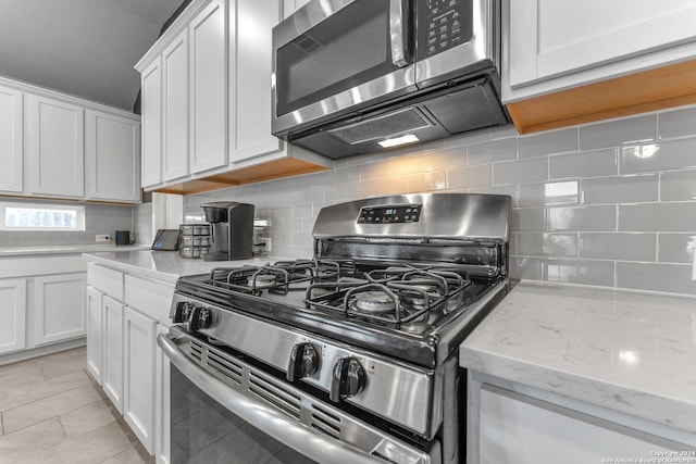 kitchen featuring light stone counters, backsplash, appliances with stainless steel finishes, white cabinetry, and light tile patterned flooring