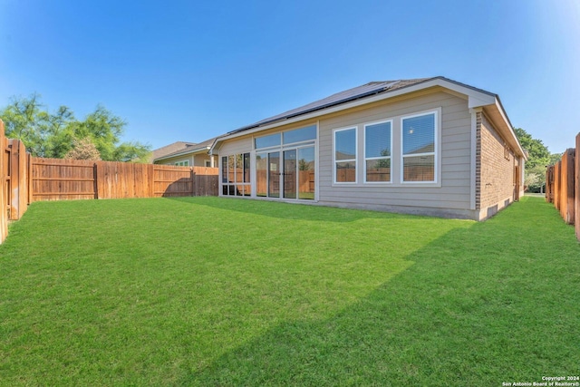 rear view of house featuring a fenced backyard, solar panels, and a yard