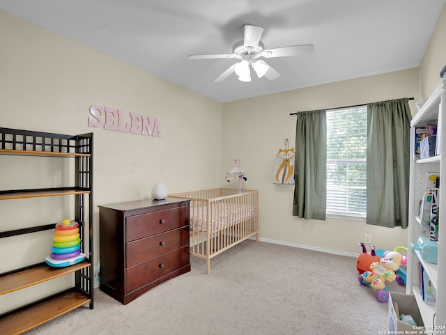 bedroom with ceiling fan, a nursery area, and light colored carpet