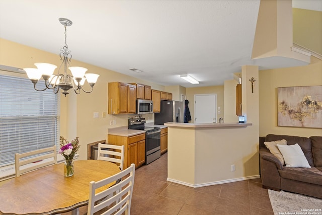 kitchen with pendant lighting, an inviting chandelier, stainless steel appliances, dark tile patterned flooring, and kitchen peninsula