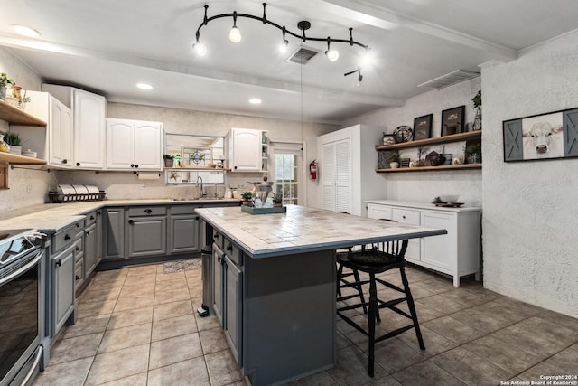 kitchen featuring gray cabinets, light countertops, open shelves, a breakfast bar area, and a sink