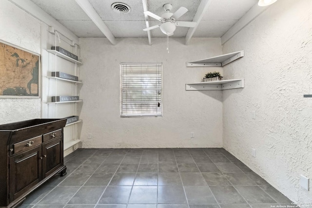 interior space featuring a textured wall, dark tile patterned floors, visible vents, and ceiling fan