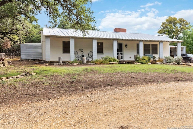view of front of property featuring a standing seam roof, concrete block siding, a porch, metal roof, and a chimney
