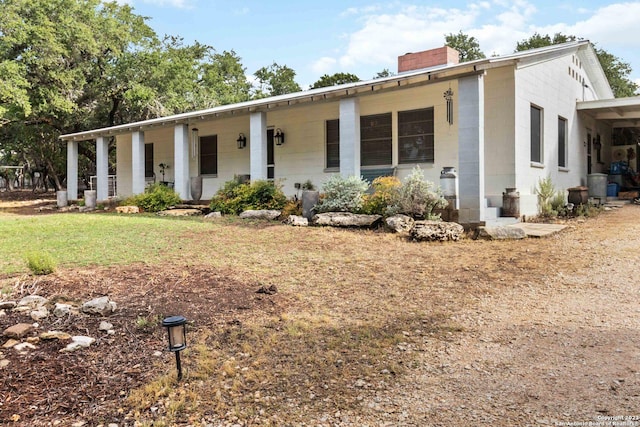 view of front facade with a chimney, covered porch, and concrete block siding