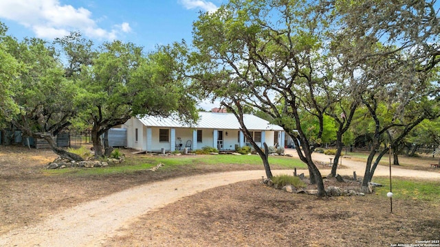 view of front of home with covered porch, fence, metal roof, and dirt driveway