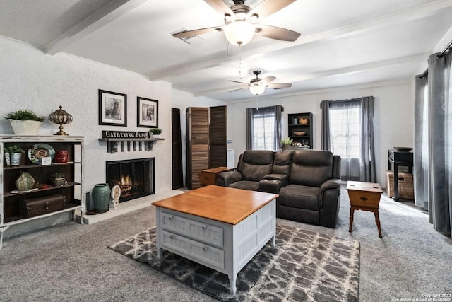 living area featuring a lit fireplace, dark colored carpet, a ceiling fan, and beam ceiling