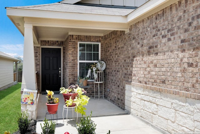 view of exterior entry featuring board and batten siding, brick siding, and a shingled roof