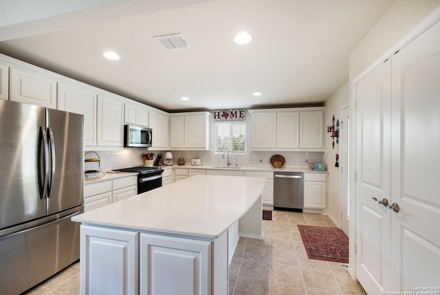 kitchen with a sink, a kitchen island, white cabinets, light countertops, and appliances with stainless steel finishes