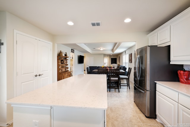 kitchen featuring a center island, light stone counters, a tray ceiling, white cabinetry, and stainless steel fridge