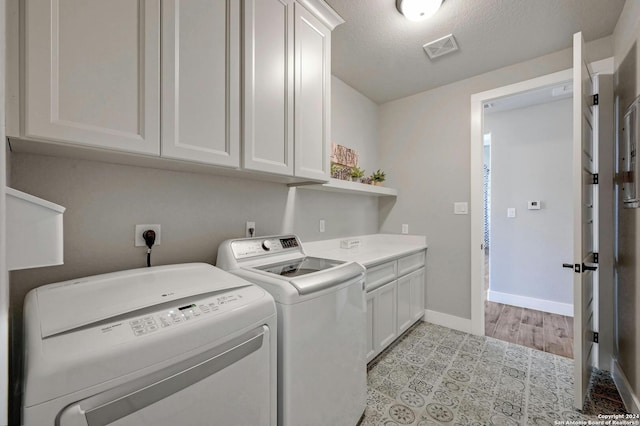 clothes washing area with light tile patterned flooring, washer and clothes dryer, a textured ceiling, and cabinets