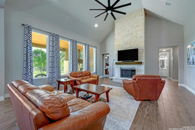 living room with ceiling fan, a stone fireplace, wood-type flooring, and high vaulted ceiling