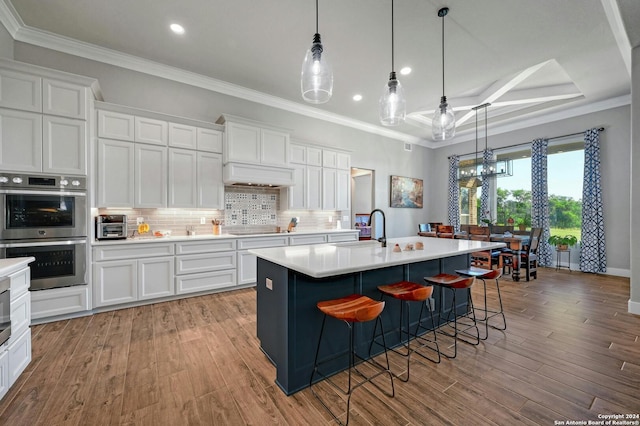 kitchen with ornamental molding, a center island with sink, light wood-type flooring, and double oven