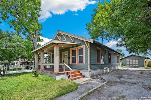 bungalow-style home with a front lawn, a porch, a garage, and an outbuilding