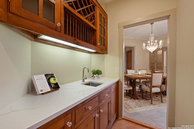 kitchen featuring a chandelier, hanging light fixtures, light stone countertops, sink, and crown molding