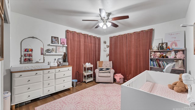 bedroom with dark hardwood / wood-style flooring, a crib, and ceiling fan