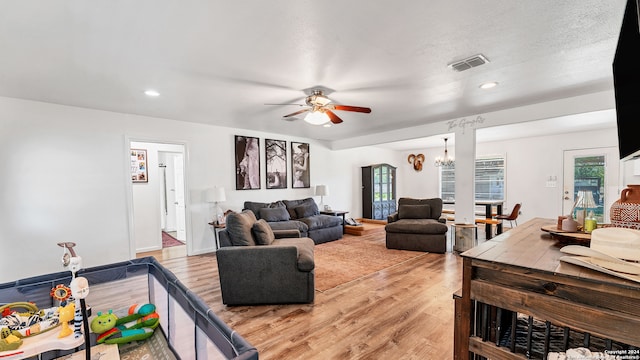 living room featuring a textured ceiling, light hardwood / wood-style flooring, and ceiling fan with notable chandelier