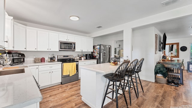 kitchen featuring light wood-type flooring, white cabinetry, light stone countertops, a center island, and stainless steel appliances