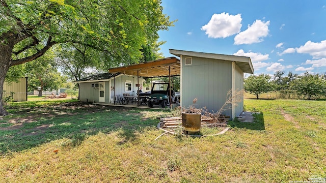 back of house with a lawn, fence, an attached carport, a pole building, and an outdoor structure