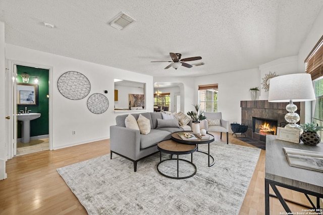 living room featuring sink, a textured ceiling, light wood-type flooring, ceiling fan, and a tiled fireplace